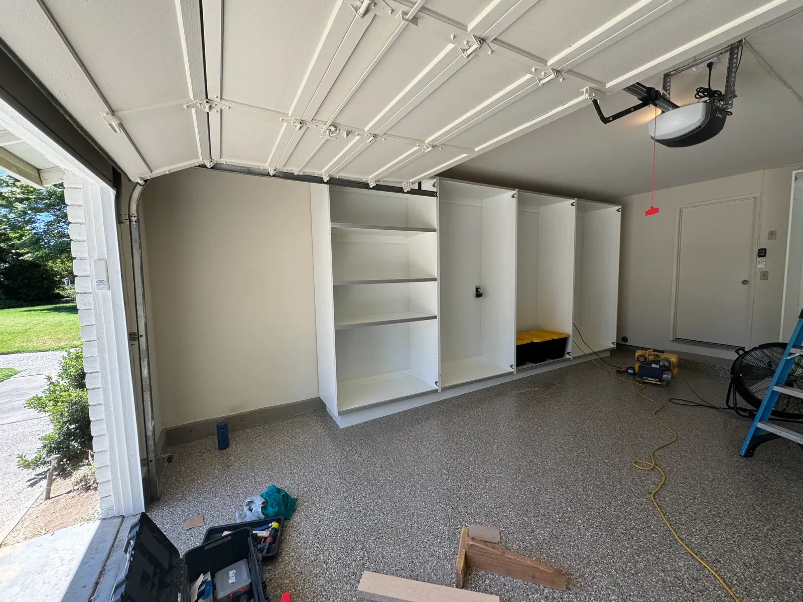 New white cabinets standing in place along a garage wall on install day, tools still out on the floor.