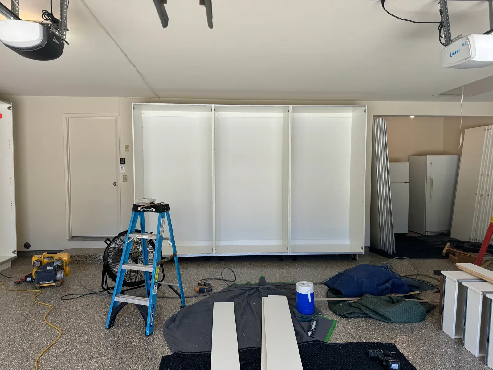 A wide run of white cabinets set against a garage wall, doors not yet hung, on install day.