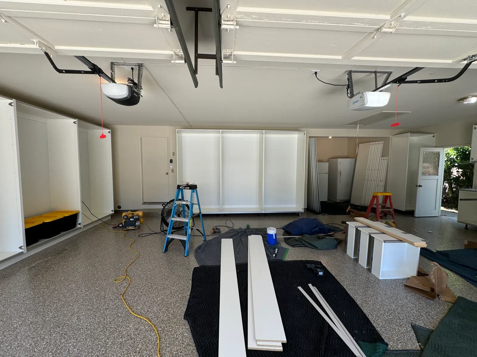 A garage part-way through an install, with cabinet runs on two walls and doors laid out on moving blankets.