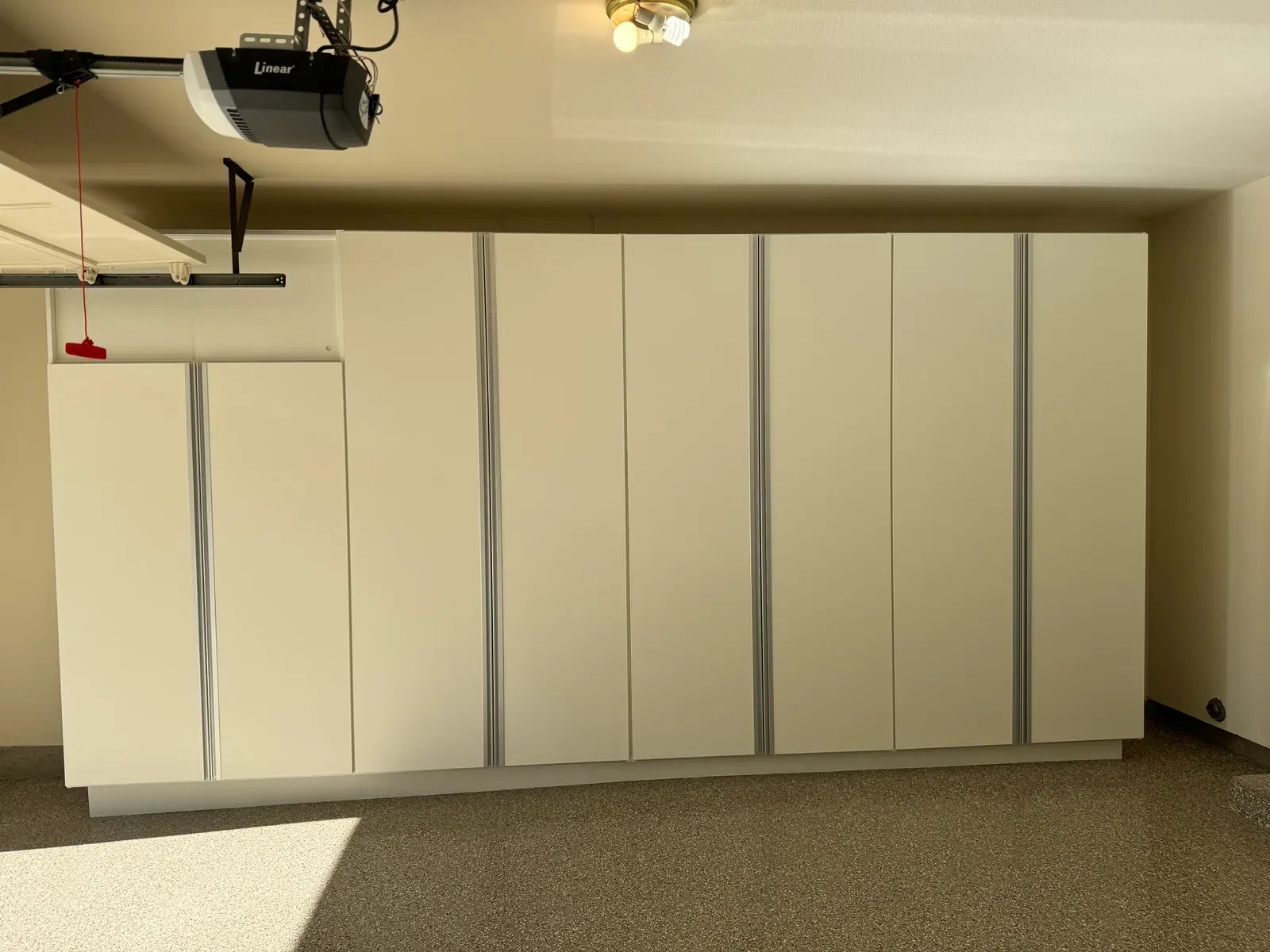 A finished wall of tall white cabinets with brushed aluminium pulls, running the full length of a garage.