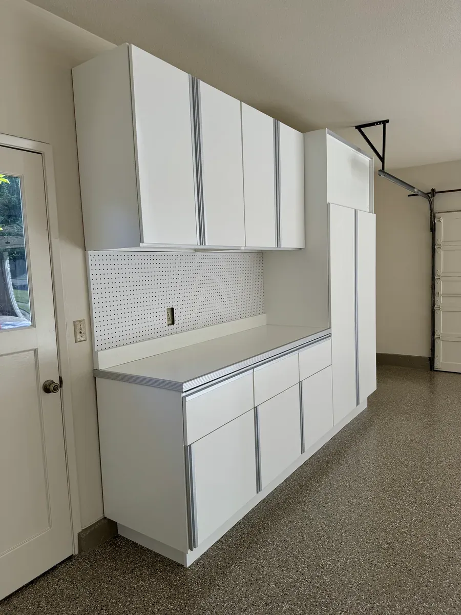 Upper cabinets over a counter with a pegboard backsplash, drawers below and a tall cabinet at the end of the run.