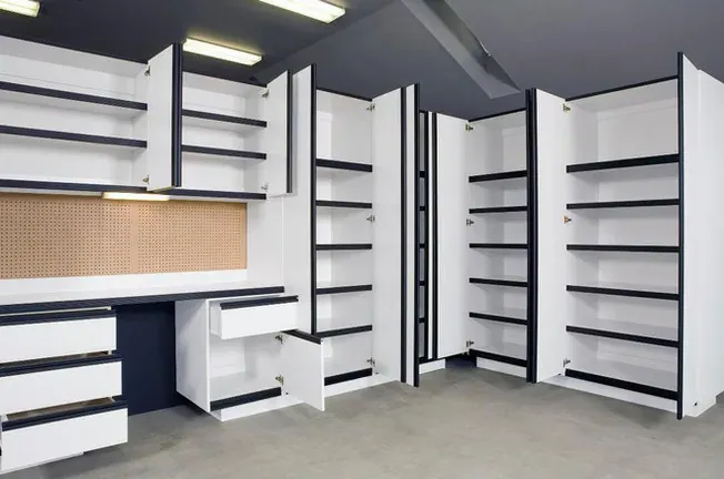A corner of white cabinets standing open, a bench with drawers below and a pegboard panel above it.